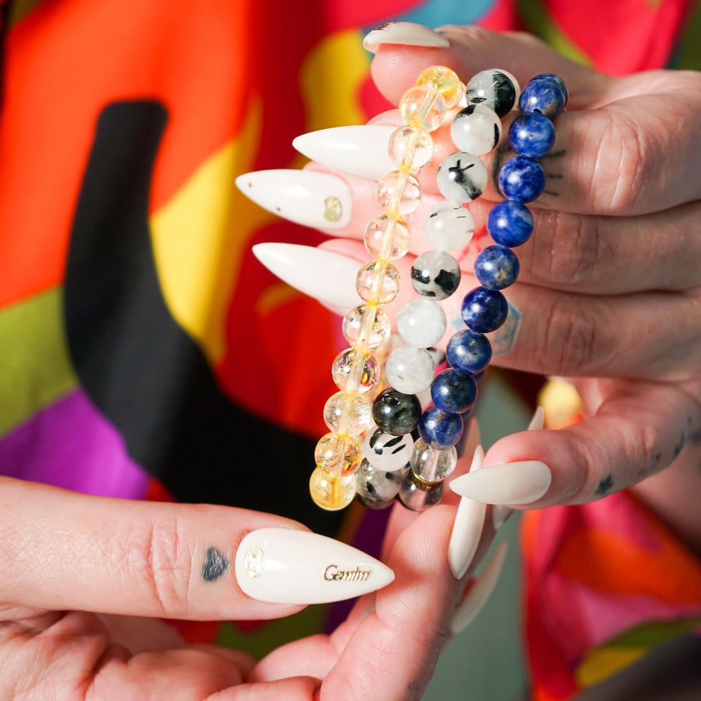 Young white woman with hand tattoos and pointed white names holding a genuine Citrine bracelet, genuine. Tourmalinated Quartz bracelet and genuine Sodalite bracelet by Energy Muse