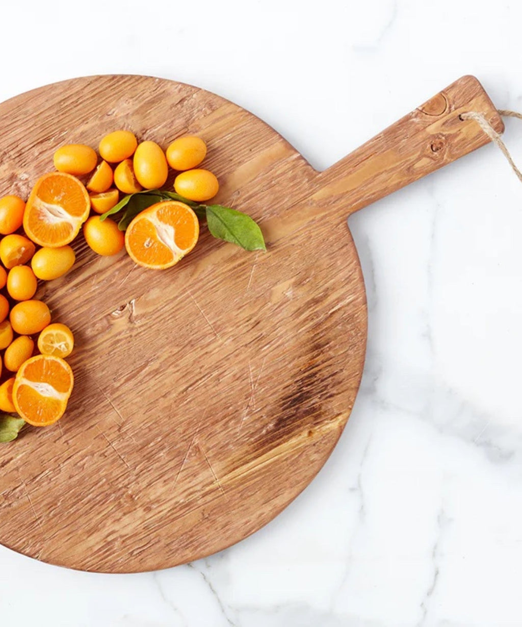 A round pine wood cutting board with a smooth surface and natural grain. It has a handle with a rope loop for hanging, conveying a rustic charm styled with sliced oranges.  | SW Home