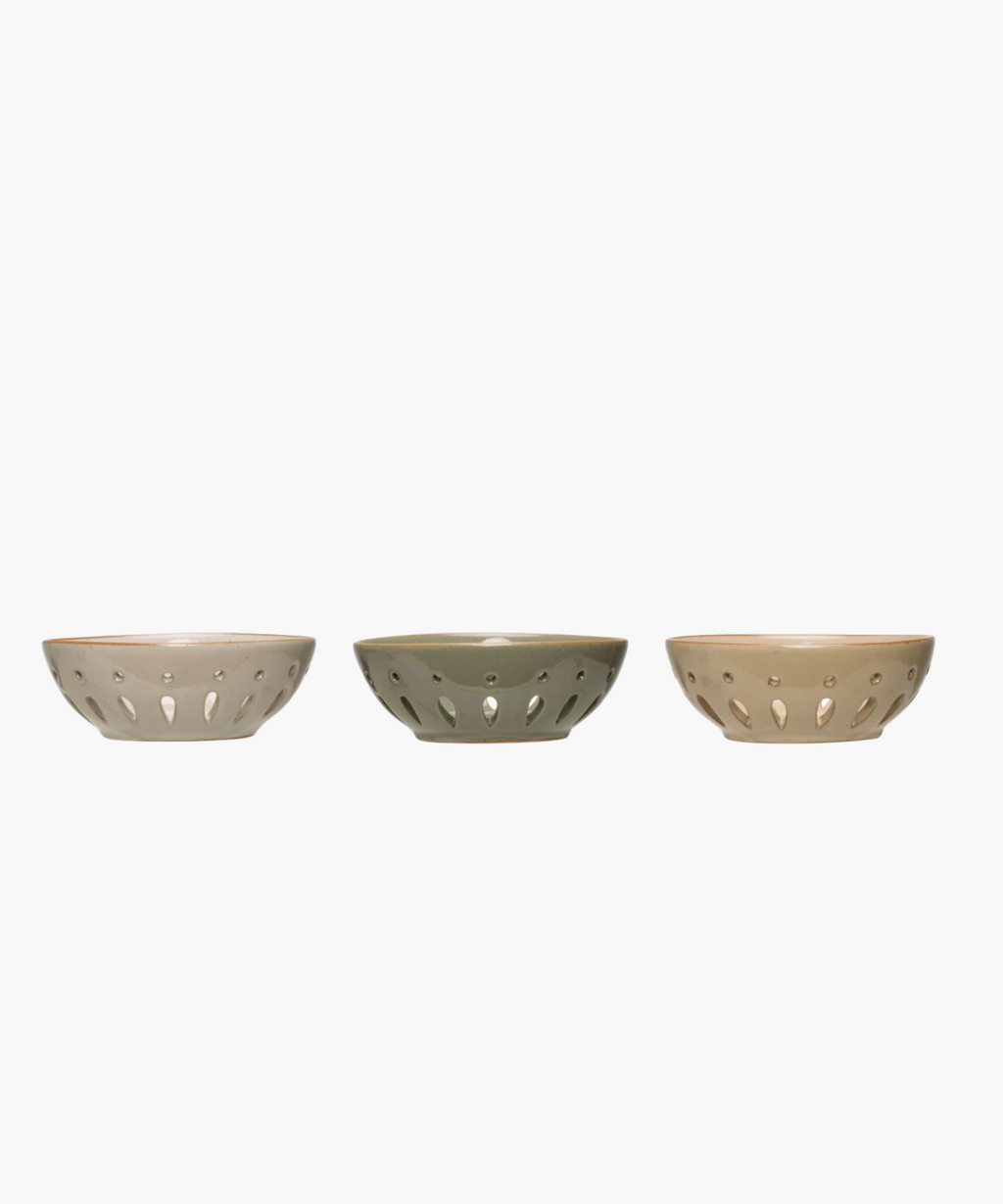 Side profile of three colanders in muted beige and gray tones are evenly spaced in a row. Each has a sleek, modern design with decorative cutout patterns. | Wildwood Home Co.