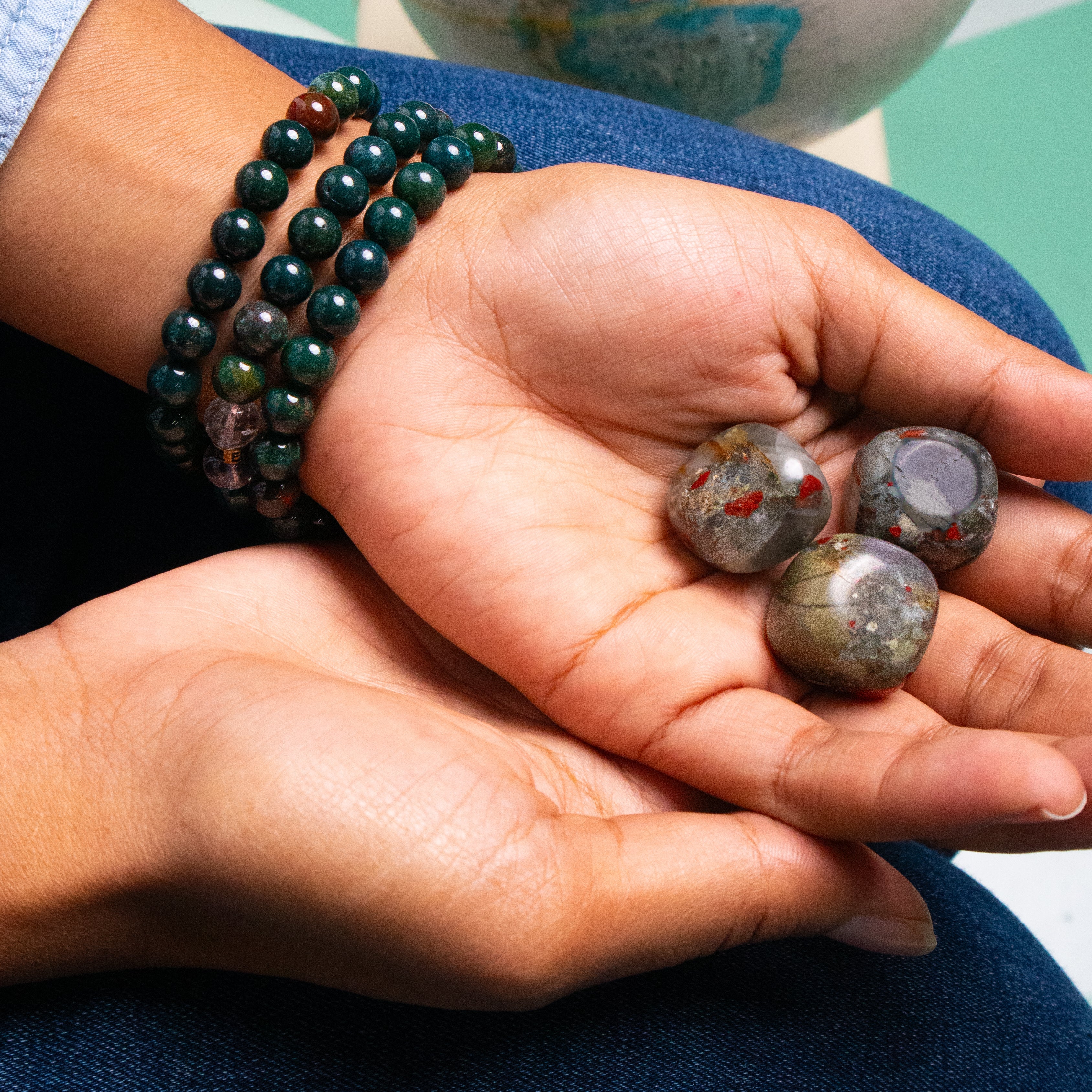 Biracial woman wearing 3 genuine Bloodstone crystal bracelets and holding 3 Bloodstone crystals in her upturned open palm by Energy Muse